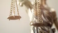 Close-up of a Lady Justice statue holding balance scales, with the chains and scale