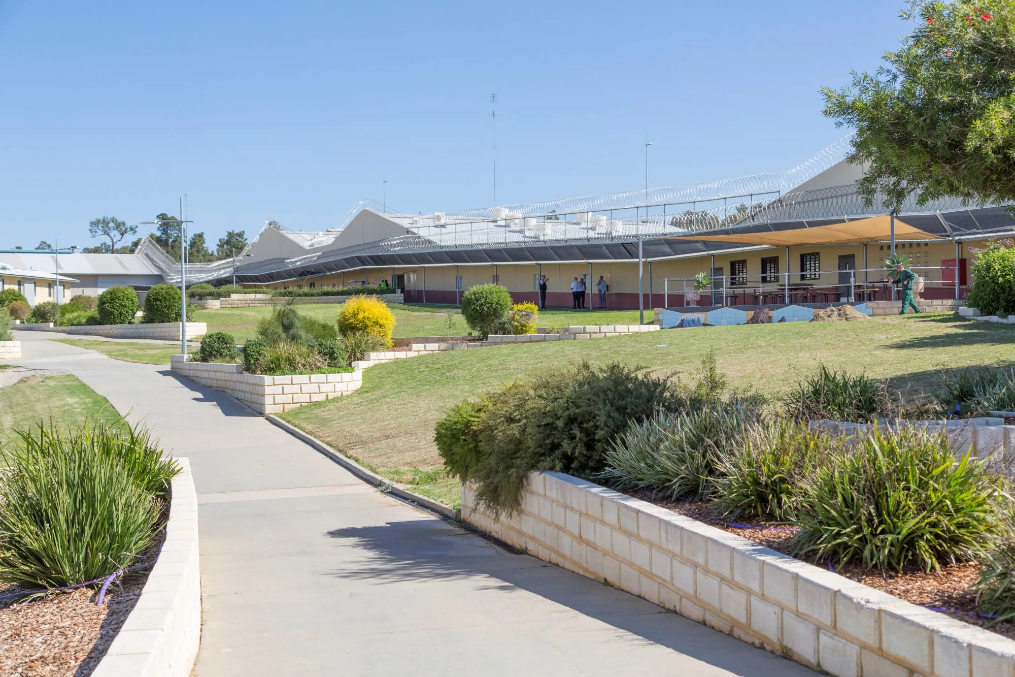 Front entrance of the prison showing a walkway with a building and grass and bushes